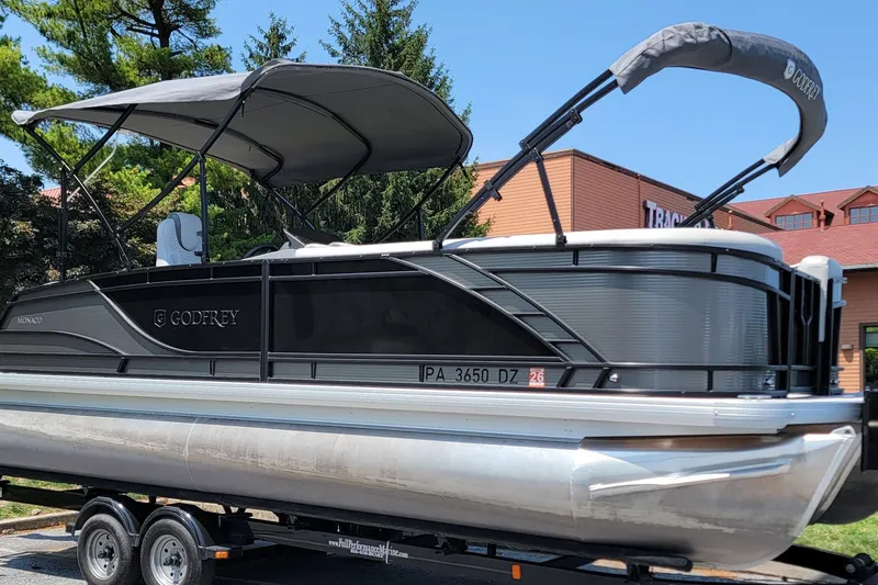 The Image of 2021 Godfrey Monaco 235 C pontoon boat on trailer, featuring sleek design and canopy. - 1