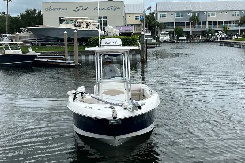 Slide: The Image of 2019 Robalo R242 Center Console boat navigating a marina with waterfront buildings. - 9