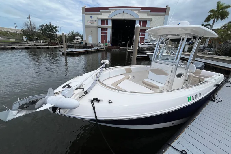 Slide: The Image of 2019 Robalo R242 Center Console boat docked at a marina with a warehouse backdrop. - 19