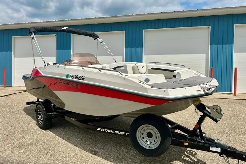 Slide: The Image of 2023 Starcraft SVX 211 IO boat on trailer, parked outside blue building. - 1