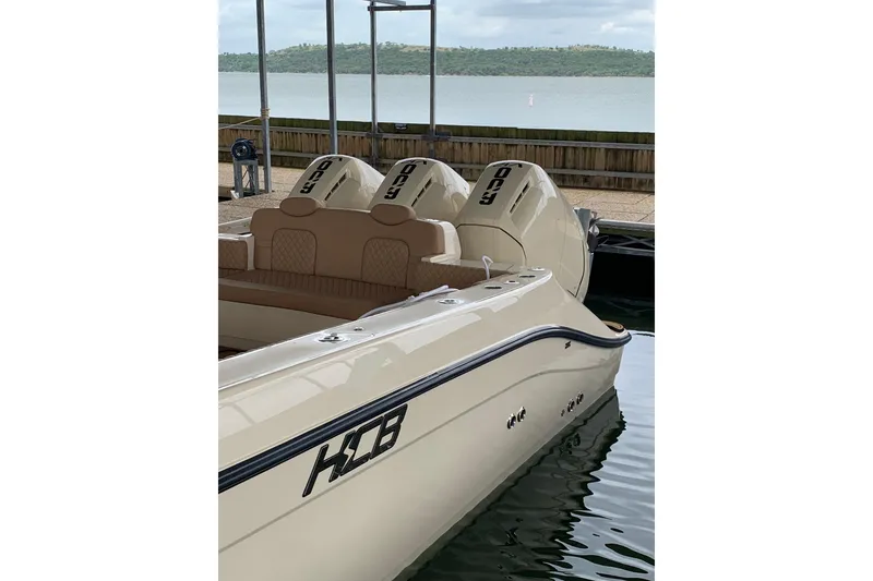 Slide: The Image of 2024 HCB 42 Lujo boat with triple outboard engines docked by a serene lake. - 82