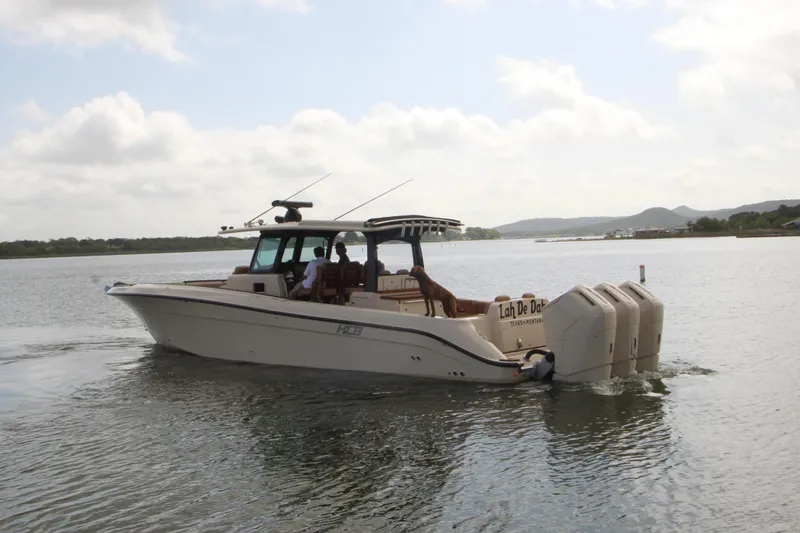 Slide: The Image of 2024 HCB 42 Lujo boat cruising on a calm lake with scenic background. - 2