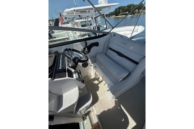 Slide: The Image of 2020 Rinker 270 Express Cruiser cockpit with steering wheel and seating, docked by the water. - 19