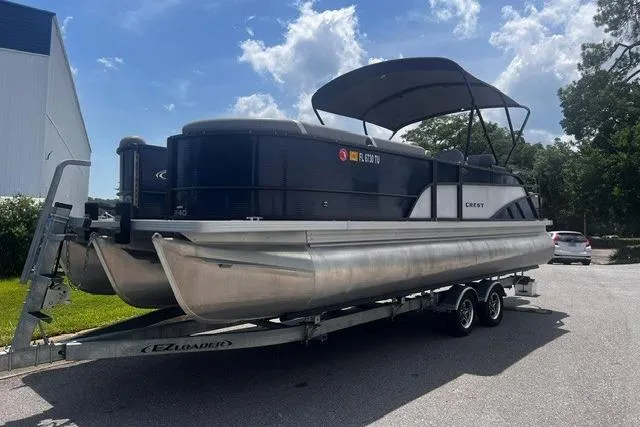 The Image of 2023 Crest Classic DLX 240 pontoon boat on trailer, parked outdoors under a blue sky. - 1