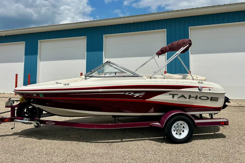 Slide: The Image of 2013 Tahoe Q4i boat on trailer, parked outside blue building under cloudy sky. - 2