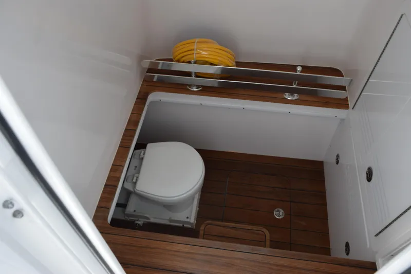 Slide: The Image of Interior of 2027 Contender 39 ST boat featuring a compact marine toilet and wooden flooring. - 18