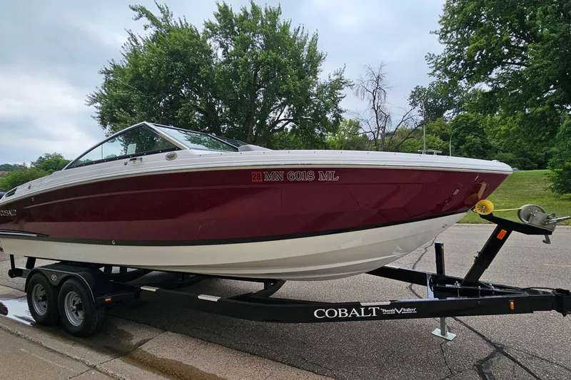 Slide: The Image of 2023 Cobalt R4 boat on trailer, parked on road with lush green trees in background. - 2