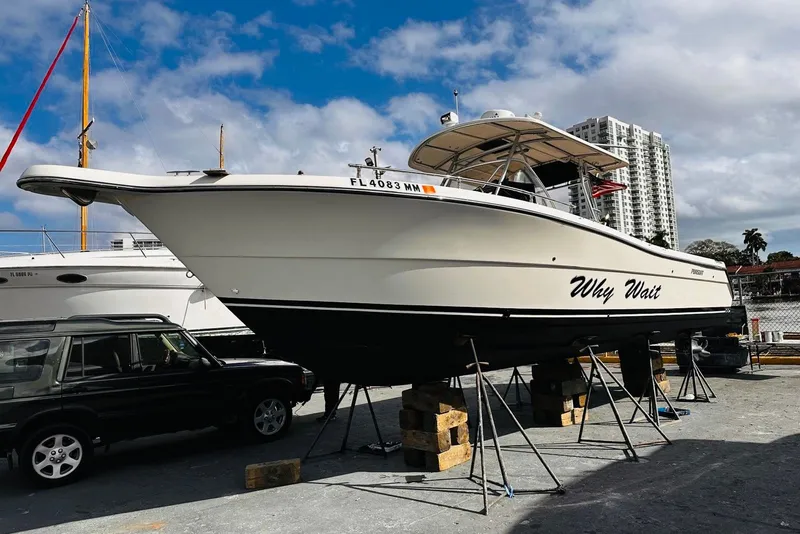 The Image of 2004 Pursuit 3070 Center Console boat named "Why Wait" on dry dock with cityscape background. - 0