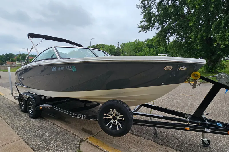 Slide: The Image of 2022 Cobalt CS23 boat on trailer, parked on a street with trees in the background. - 4