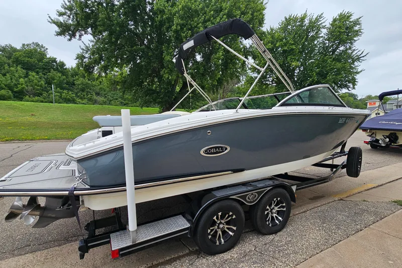Slide: The Image of 2022 Cobalt CS23 boat on trailer, parked on a road with lush greenery background. - 3