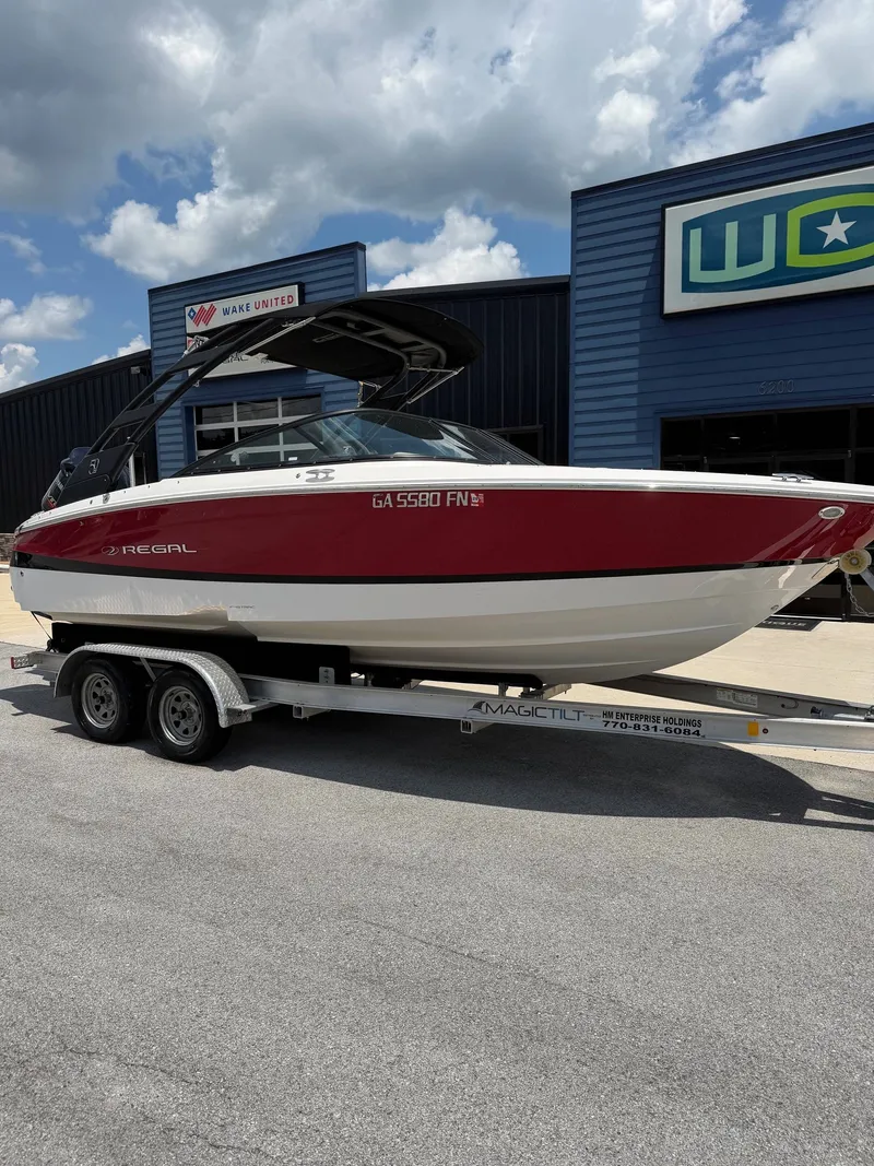 The Image of A 2021 Regal LX2 boat on a trailer in front of a blue building. - 1