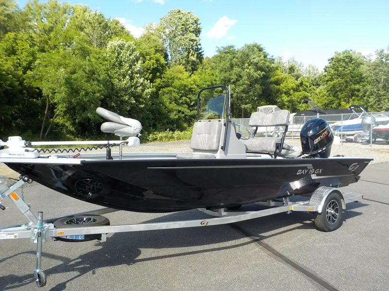 Slide: The Image of The image shows a black G3 Bay 19 GX boat on a trailer, surrounded by trees. - 2