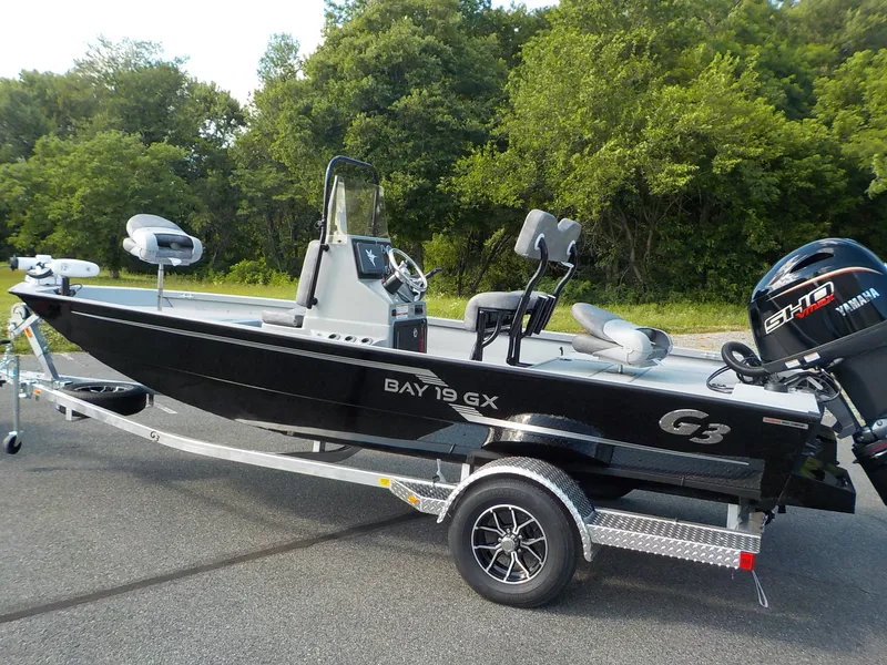 Slide: The Image of The image shows a black G3 Bay 19 GX boat on a trailer, surrounded by trees. - 3