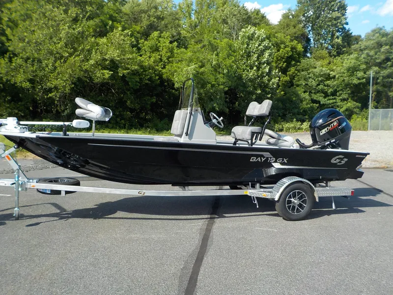 The Image of A black 2026 G3 Bay 19 GX boat on a trailer, surrounded by trees. - 1