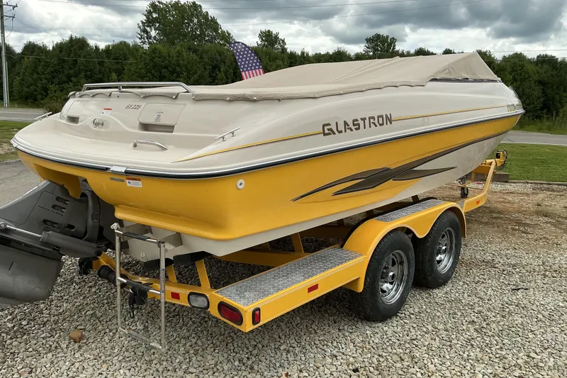 Slide: The Image of 2003 Glastron GX225 boat on trailer, yellow hull, covered, parked on gravel. - 3