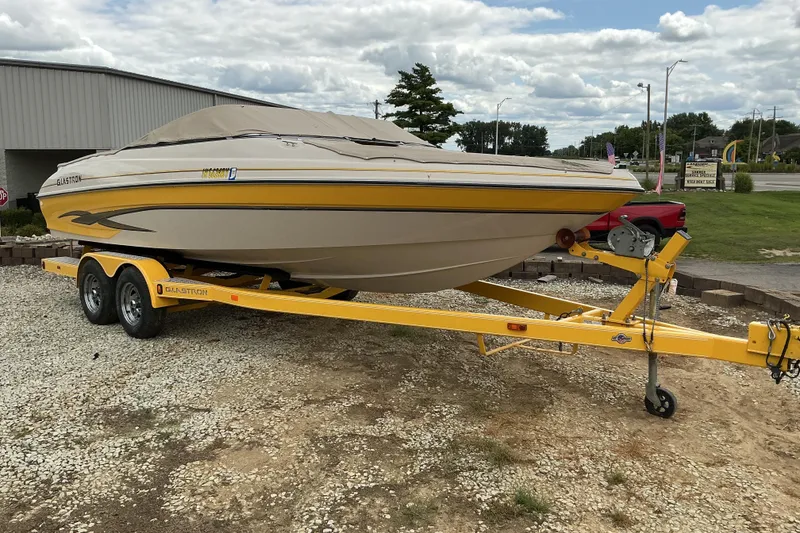 Slide: The Image of 2003 Glastron GX225 boat on a yellow trailer, parked outdoors on gravel. - 10