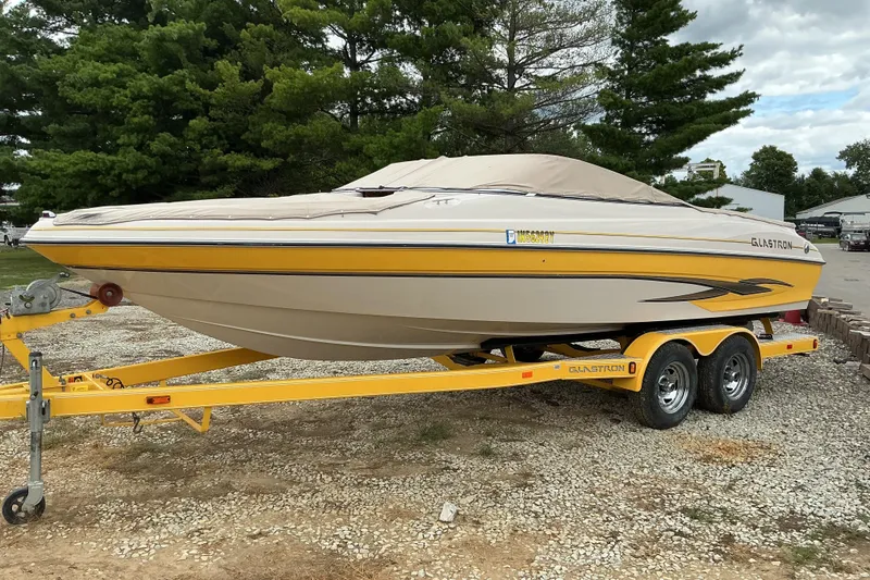 The Image of 2003 Glastron GX225 boat on trailer, covered, parked outdoors with trees in background. - 1