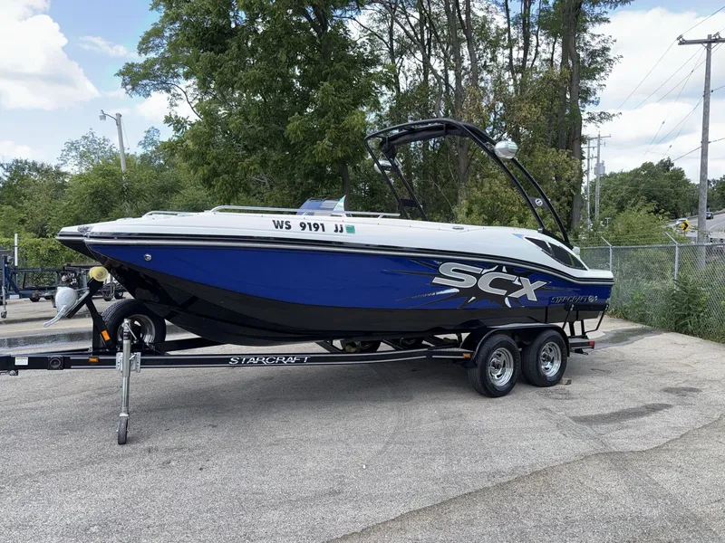 Slide: The Image of A blue and white 2015 Starcraft 211 SCX boat on a trailer in a parking area. - 13