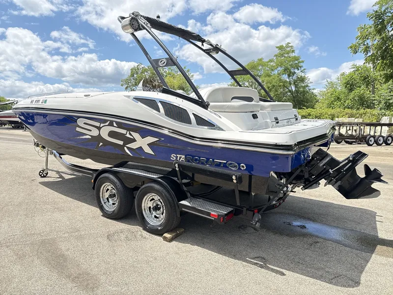 Slide: The Image of A 2015 Starcraft 211 SCX boat on a trailer. It features a sleek design and is blue and white. - 6