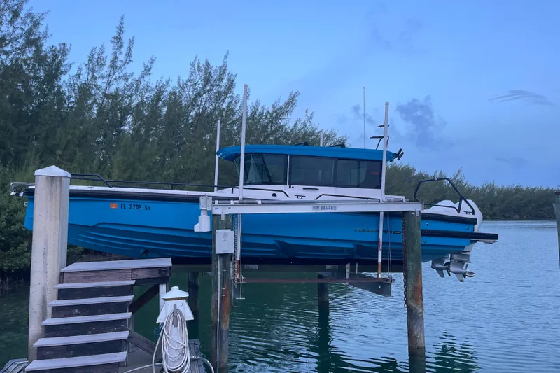 The Image of 2021 Axopar 28 Cabin boat docked on lift, surrounded by serene water and trees. - 0