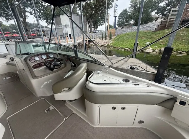Slide: The Image of The image shows the cockpit of a 2006 Sea Ray 240 Sundeck boat. It features a steering wheel, instrument panels, and beige upholstery. A dock is visible in the background. - 15