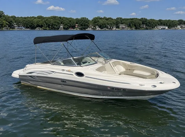 The Image of 2006 Sea Ray 240 Sundeck on a calm lake with a Bimini top and spacious deck. - 1
