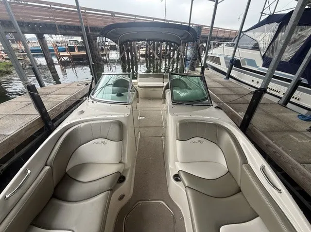 Slide: The Image of A 2006 Sea Ray 240 Sundeck with beige seating and a black bimini top, docked at a marina. - 12