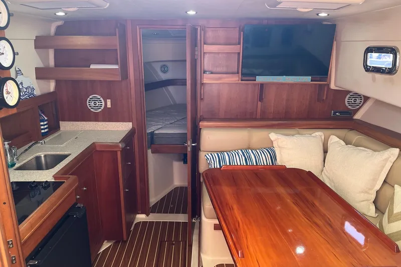 Slide: The Image of 2007 Mainship Pilot 34 Sedan interior with wood finishes, kitchenette, and cozy seating area. - 10