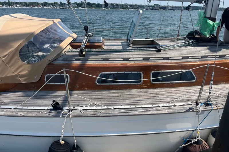 The Image of 1984 Vindo 34 sailboat with wooden deck and beige canopy, docked by the water. - 1