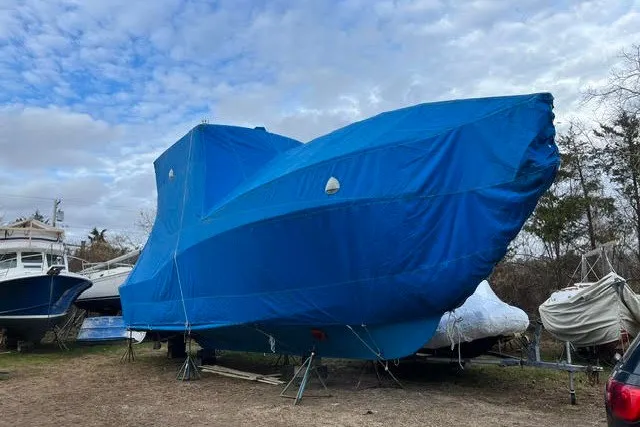 Slide: The Image of 1987 Fortier 40 boat covered in blue tarp, stored outdoors under a cloudy sky. - 21