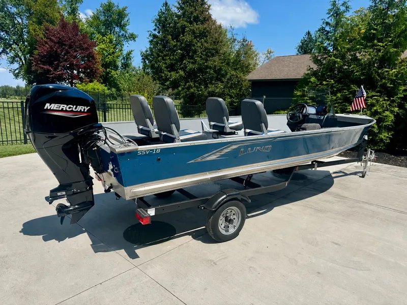 The Image of A 2025 Lund SSV-18 boat on a trailer, featuring a Mercury outboard motor and four seats. - 0