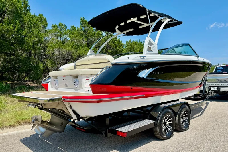 Slide: The Image of 2017 Cobalt A25 boat on trailer, black and red design, parked near trees. - 20