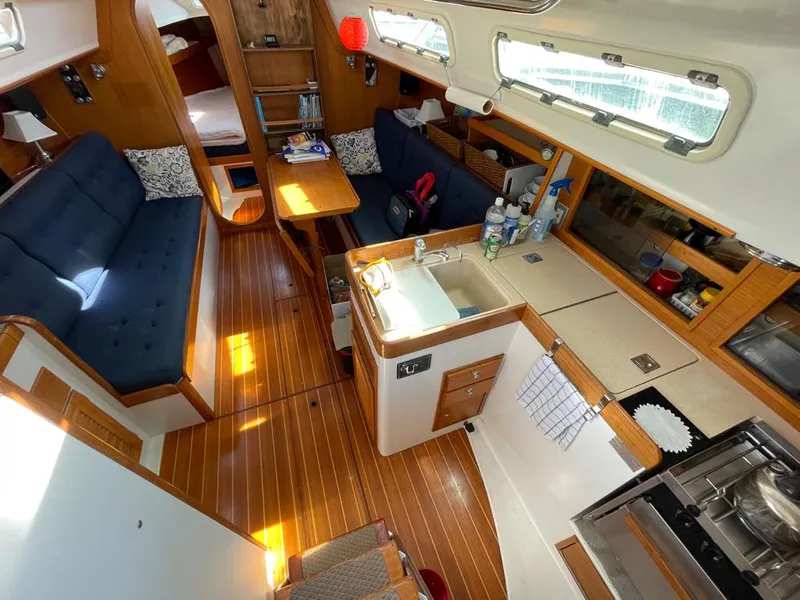 Slide: The Image of Interior of a 2001 J/32 with wooden floors, blue upholstery, and a small kitchen area. - 16