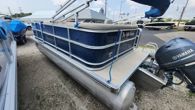 Slide: The Image of A blue pontoon boat with a Yamaha engine sits on a gravel lot next to other boats. - 3