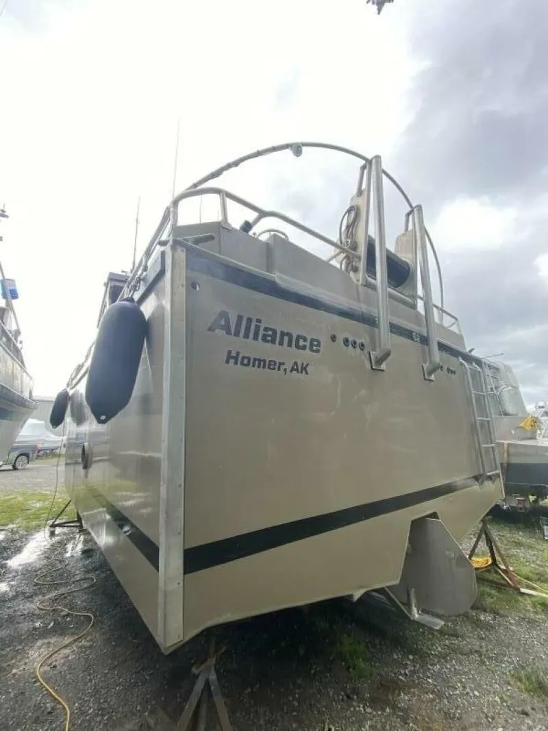 Slide: The Image of The image shows a 2022 Custom Freestyle Marine 32 boat on a gravel lot. It has a silver exterior and is equipped with fenders. The name "Alliance" and location "Homer, AK" are visible on the back. - 39