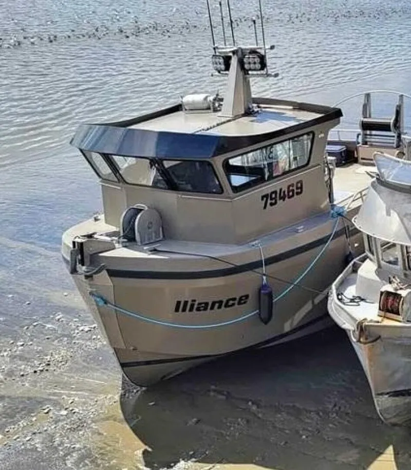 Slide: The Image of A modern boat with a gray hull is docked at the shore. It features an enclosed cabin and fishing rod holders. - 2