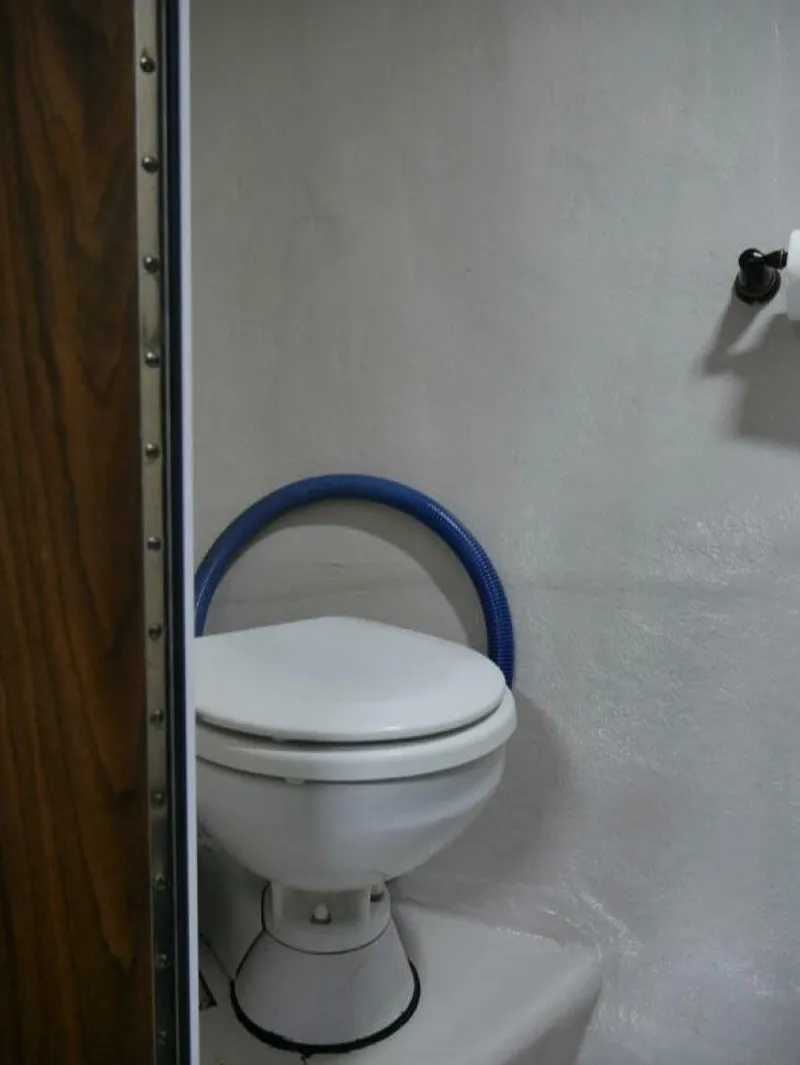 Slide: The Image of The image shows a toilet in a boat, surrounded by white walls and a blue hose. - 34