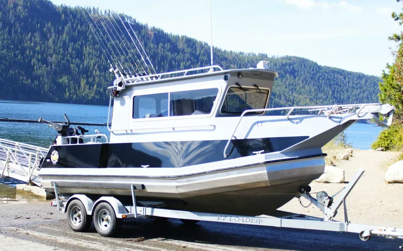 Slide: The Image of A 2005 ACB 27 boat on a trailer by a lake with forested hills. - 2