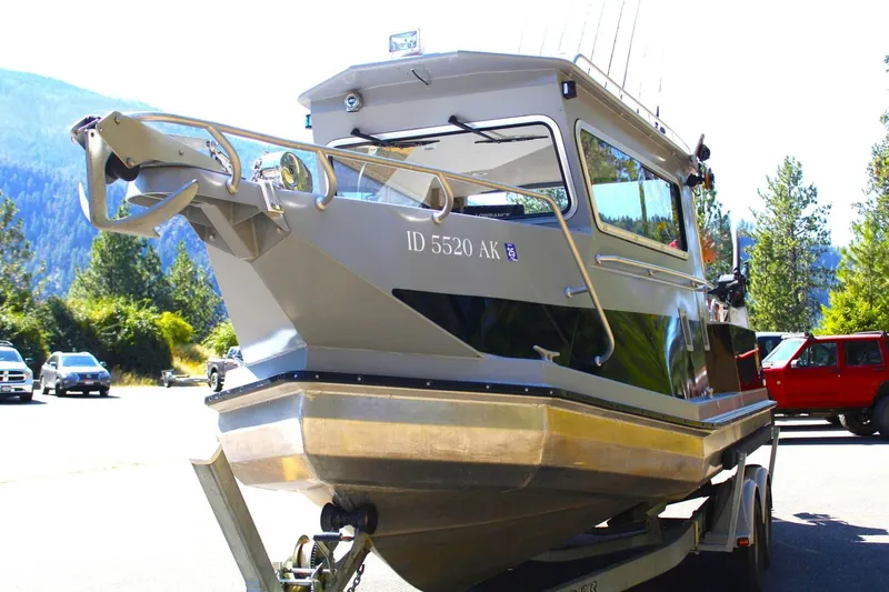 Slide: The Image of A silver 2005 ACB 27 boat on a trailer in a parking lot, surrounded by trees. - 49