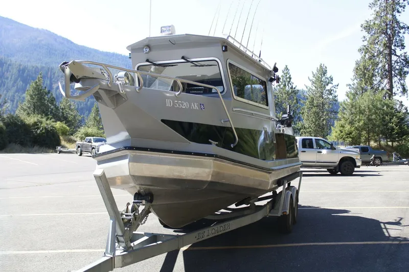 Slide: The Image of A silver boat on a trailer in a parking lot, surrounded by trees and mountains. - 11