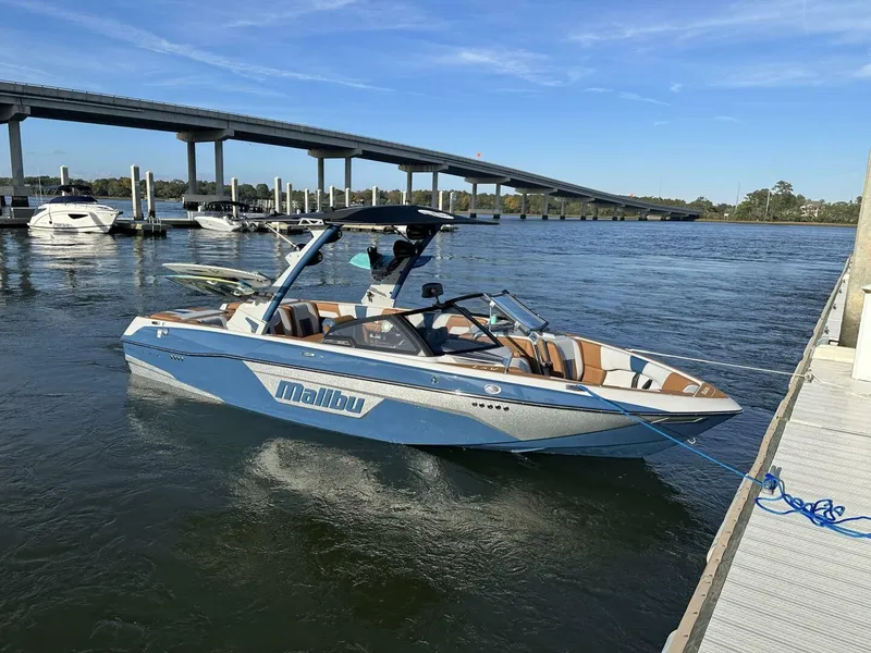 Slide: The Image of A blue and white 2023 Malibu Wakesetter 23 LSV is docked. A bridge is visible in the background. - 10