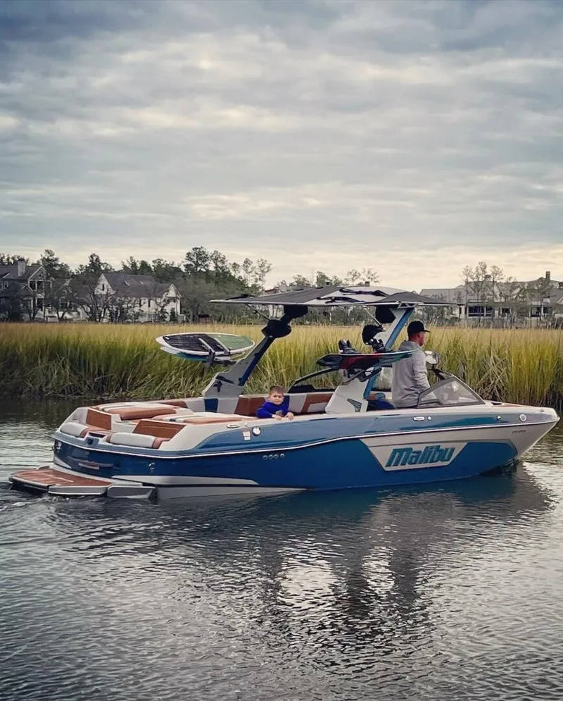 Slide: The Image of A 2023 Malibu Wakesetter 23 LSV on calm water, surrounded by reeds and houses. - 3