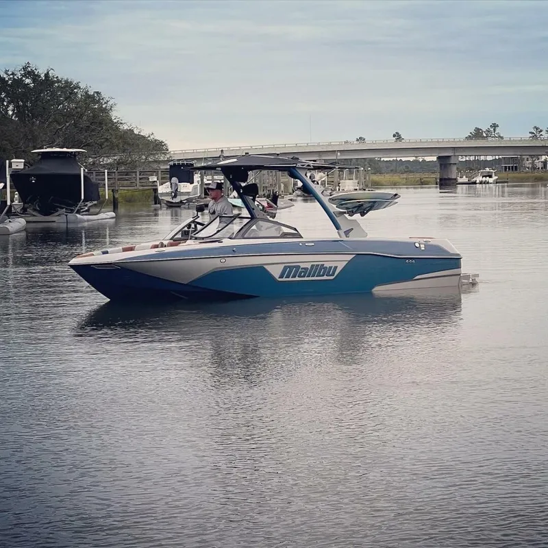 Slide: The Image of A 2023 Malibu Wakesetter 23 LSV in blue and white on calm water, with a bridge in the background. - 5