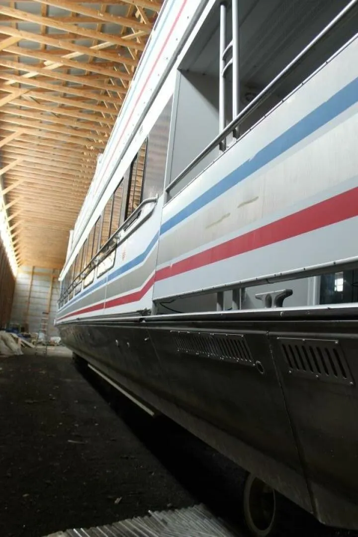 Slide: The Image of A 2000 Sumerset 75 Houston houseboat in a warehouse. It features colorful stripes on the side. - 20