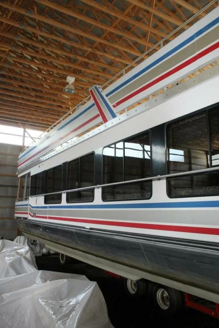 Slide: The Image of A 2000 Sumerset 75 Houston houseboat in a storage facility. It features a distinctive stripe design. - 7