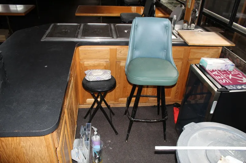 Slide: The Image of The kitchen of a houseboat with wooden cabinets, a green bar stool, and a small refrigerator. - 38