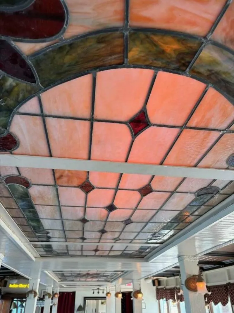 Slide: The Image of A colorful stained glass window adorns the ceiling of a boat, surrounded by white columns. - 24