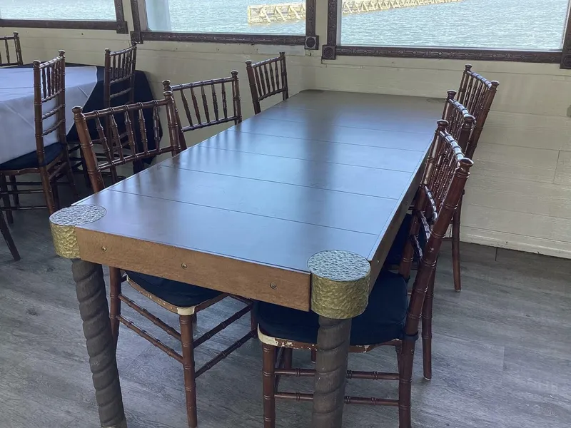 Slide: The Image of A long wooden table with chairs is set in a room overlooking the water. - 36