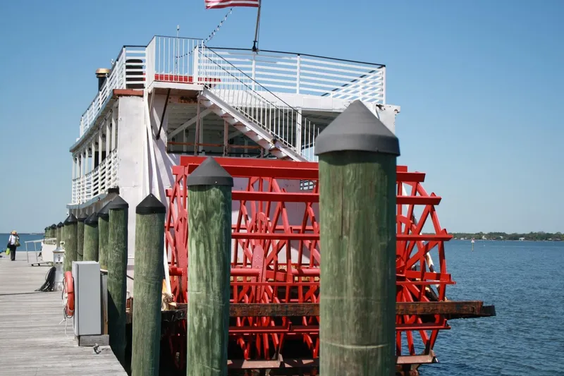 Slide: The Image of A historic paddle wheel boat docked at a wooden pier. An American flag waves in the breeze. - 13