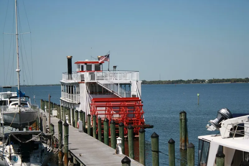 Slide: The Image of A white paddle wheel boat with a red wheel is docked at a wooden pier. - 10